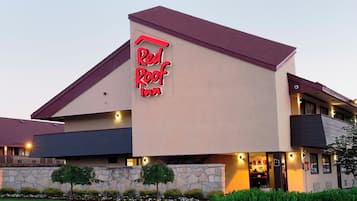 Un Red Roof Inn con fachada de piedra, techo plano y una entrada bien iluminada.