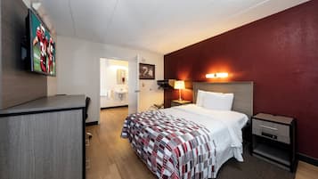 A hotel room with a bed, bedside table, lamp, and a TV mounted on the wall.