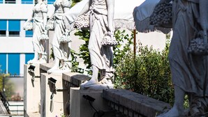 Eine Reihe klassischer Statuen auf einer Steinbalustrade, im Hintergrund ein modernes Gebäude.