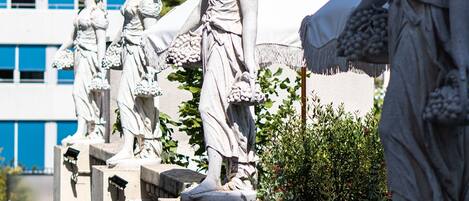 A series of classical statues on a stone balustrade with a modern building in the background.