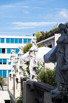A series of classical statues on a stone balustrade with a modern building in the background.