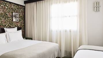 A hotel room with a large bed, a smaller bed, a window with curtains, and a wall with a floral wallpaper.