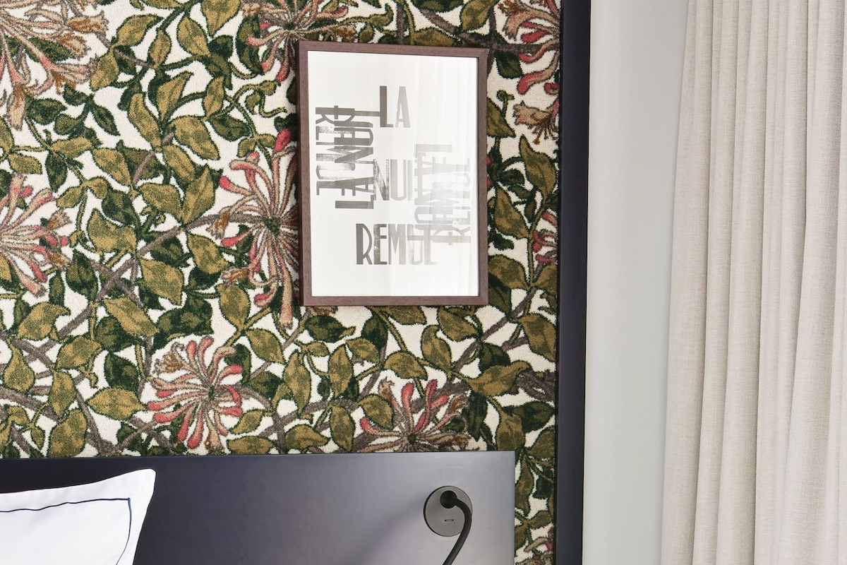 A neatly made bed with white linens, a green nightstand with a lamp, and a framed picture on the wall.