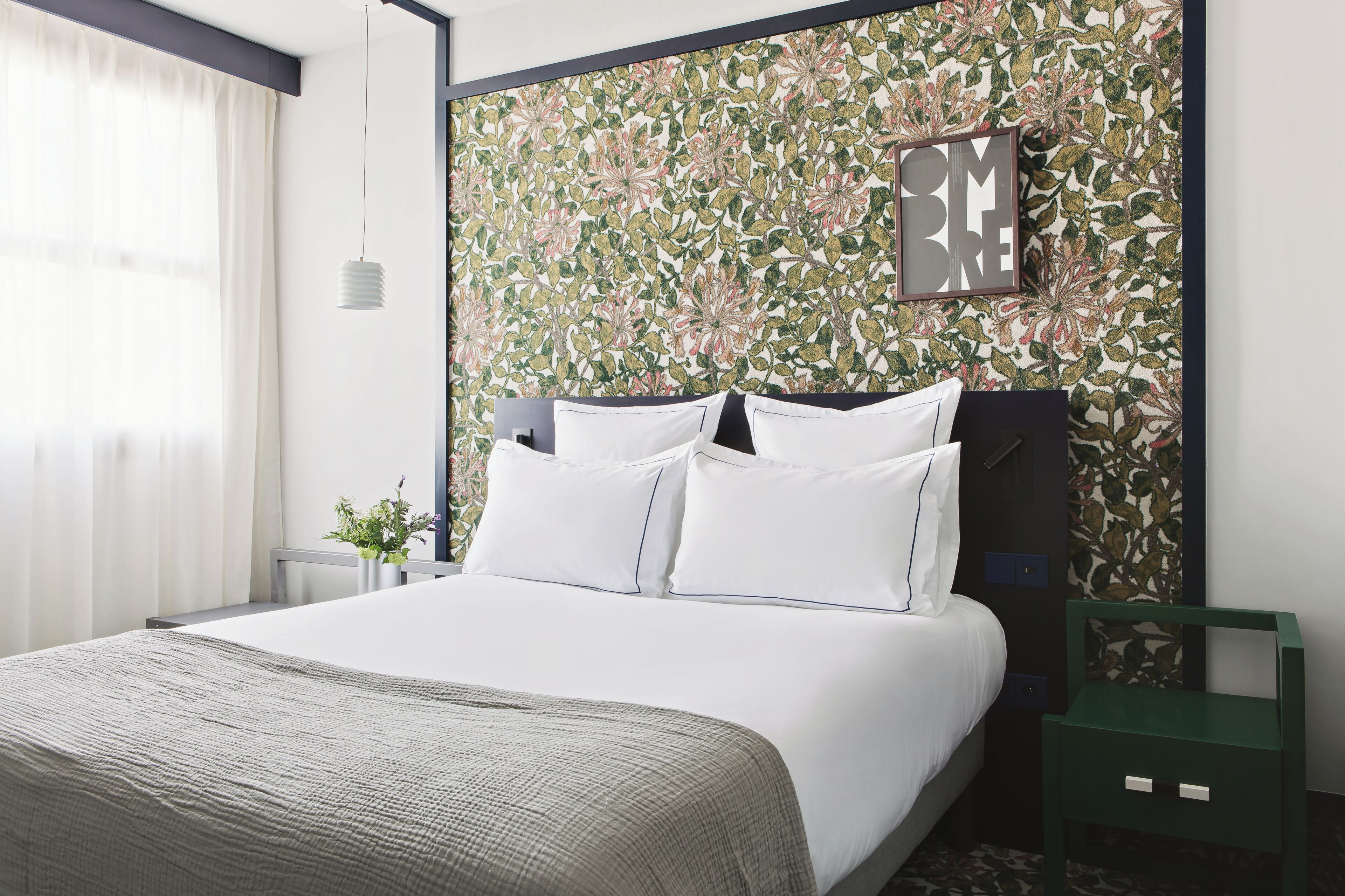 A neatly made bed with white linens, a green nightstand, and a floral-patterned headboard.