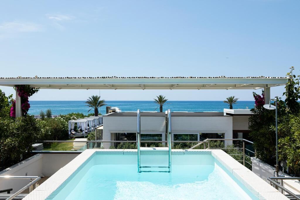 A swimming pool with a view of the sea, a covered area, and a modern building in the background.