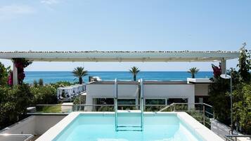 A swimming pool with a view of the sea, a covered area, and a modern building in the background.