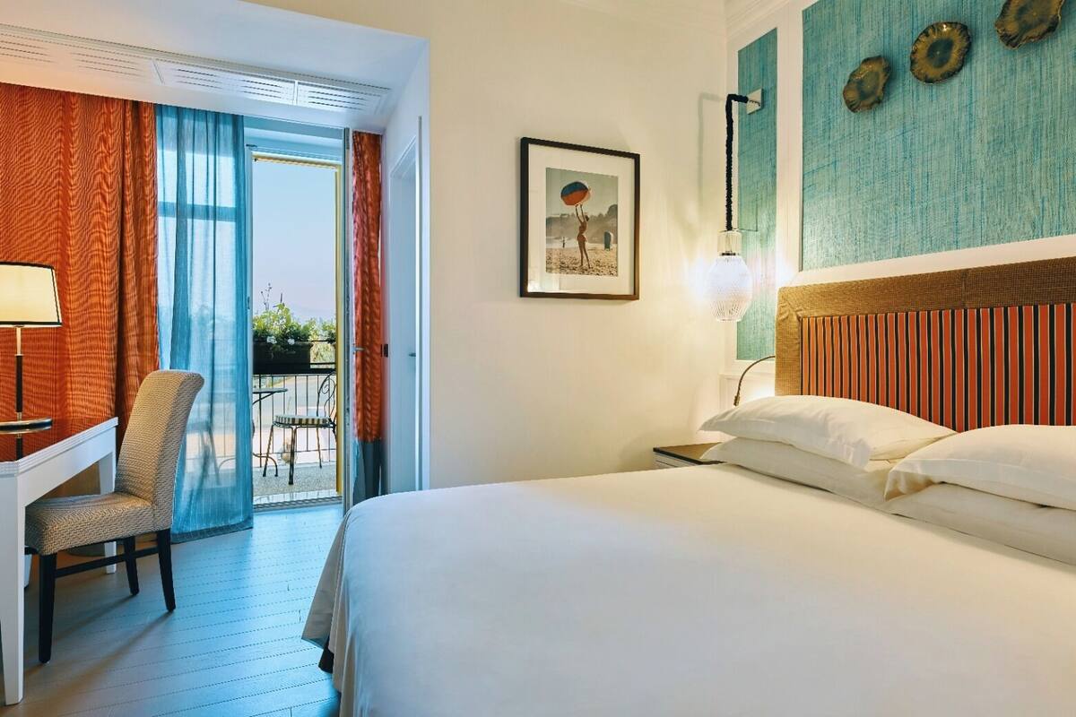 Une chambre d’hôtel comprenant un lit, un bureau, une chaise, un balcon avec vue et un mur décoré d’assiettes.