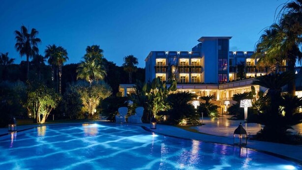 Ein Hotel mit Pool, Palmen und beleuchteter Fassade bei Nacht.