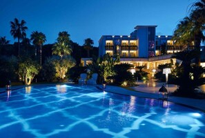 A hotel with a swimming pool, palm trees, and a well-lit exterior at night. - Boutique Hotel Esplanade (Capaccio-Paestum)