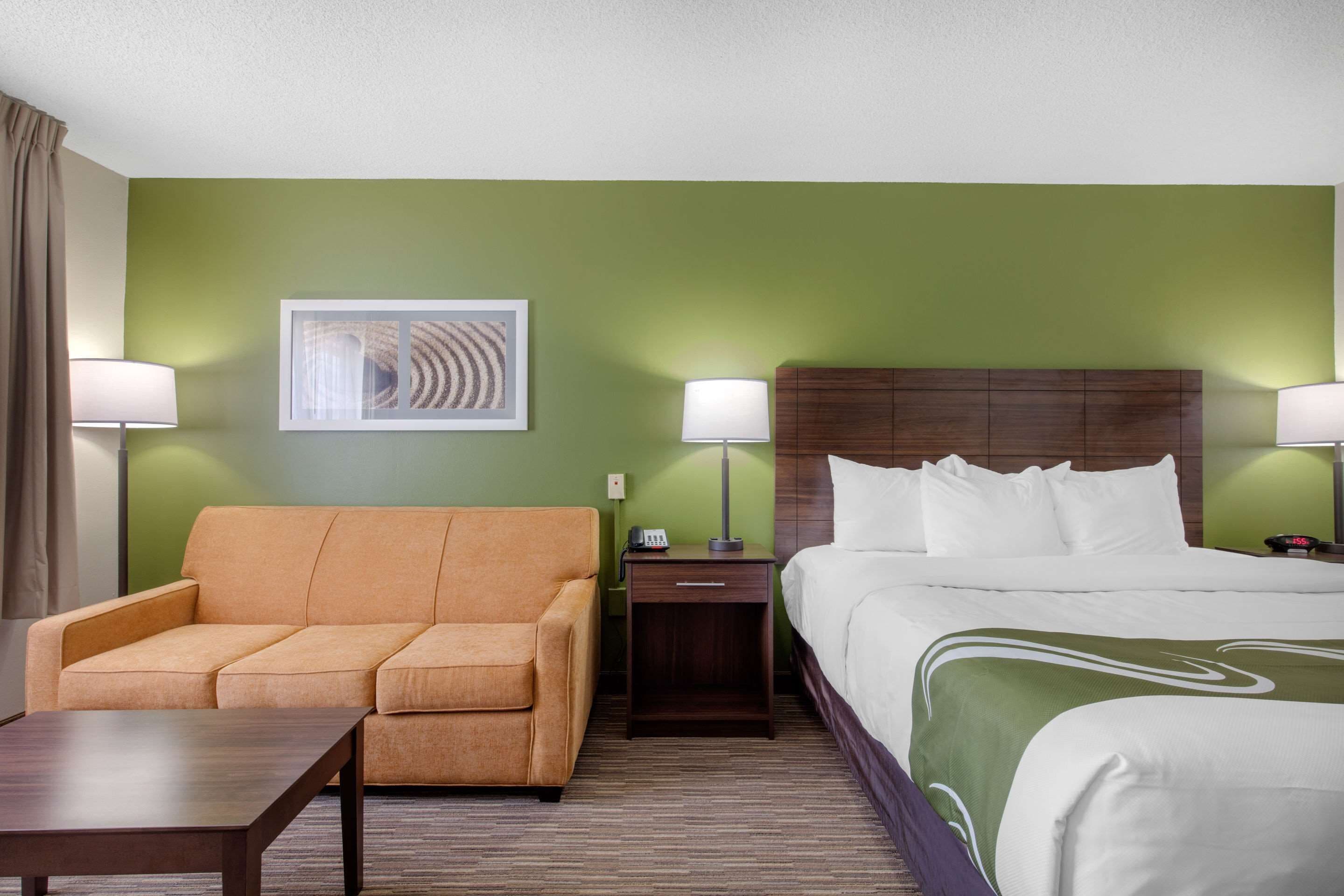 A hotel room with a green wall, a sofa, a bed with white bedding, two bedside tables with lamps, and a framed picture on the wall.