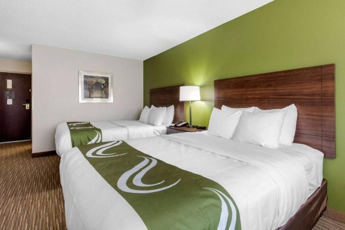 A hotel room with two beds, a green wall, a wooden headboard, a lamp, and a framed picture on the wall.