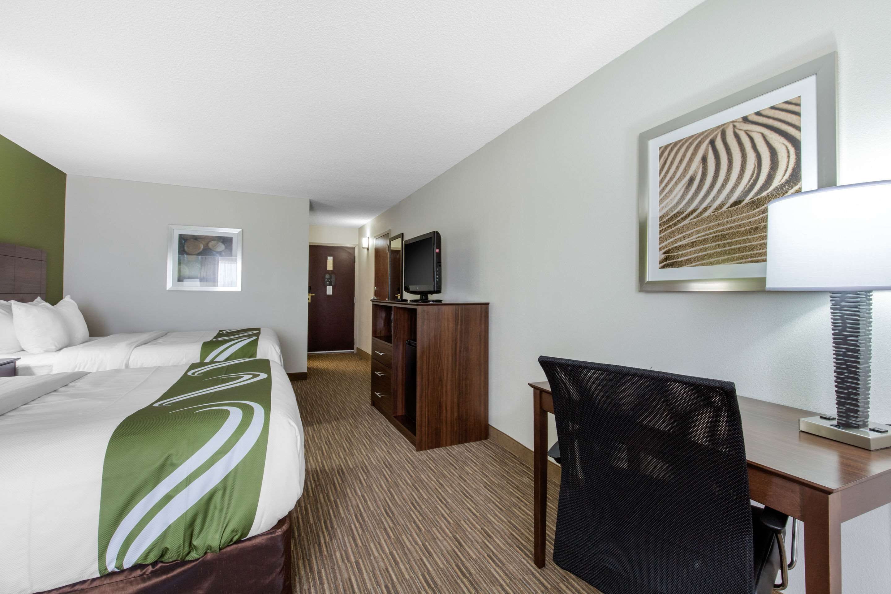 Habitación de hotel con cama, escritorio, silla, televisor y un cuadro en la pared.