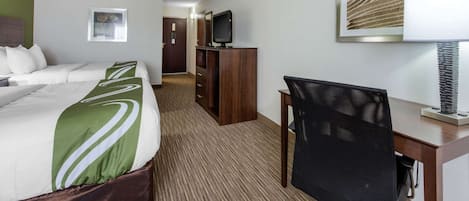 Habitación de hotel con cama, escritorio, silla, televisor y un cuadro en la pared.