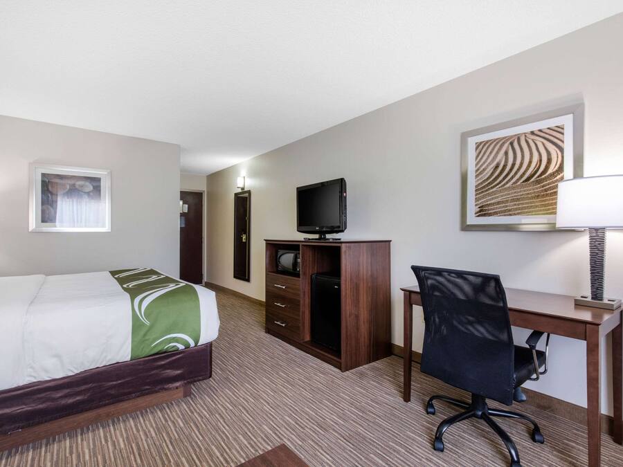 Ein Hotelzimmer mit Bett, Schreibtisch, Stuhl, Fernseher und Lampe.