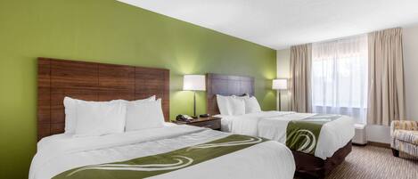 Hotelkamer met twee bedden, een groene muur, een houten hoofdeinde, een nachtkastje, een lamp, een stoel en een raam met gordijnen.