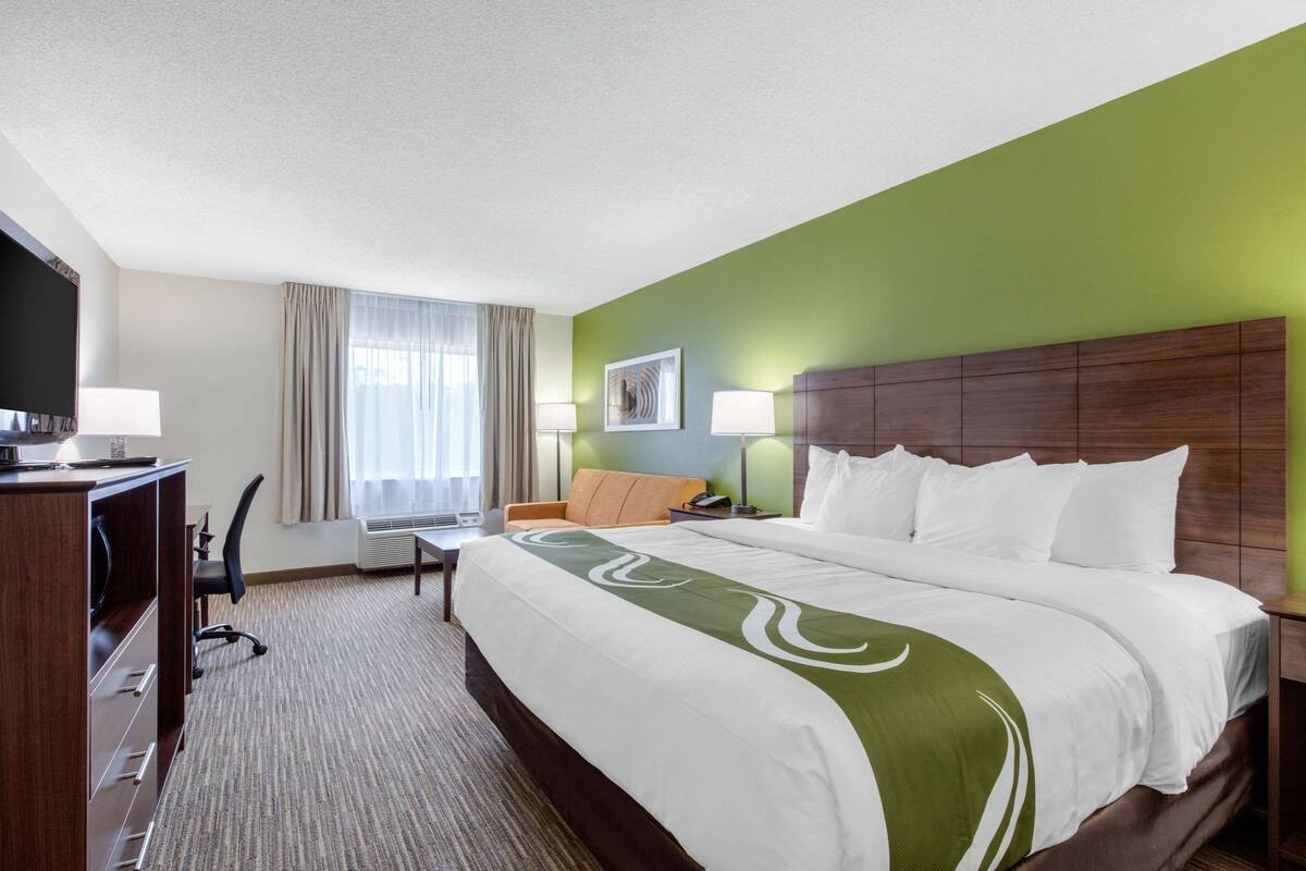 A hotel room with a large bed, a desk with a chair, a television, and a window with curtains.