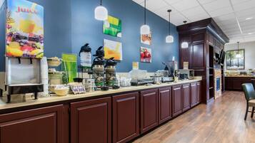 Un buffet pour le petit-déjeuner avec des distributeurs de jus, des machines à café et une variété d'aliments pour le petit-déjeuner.