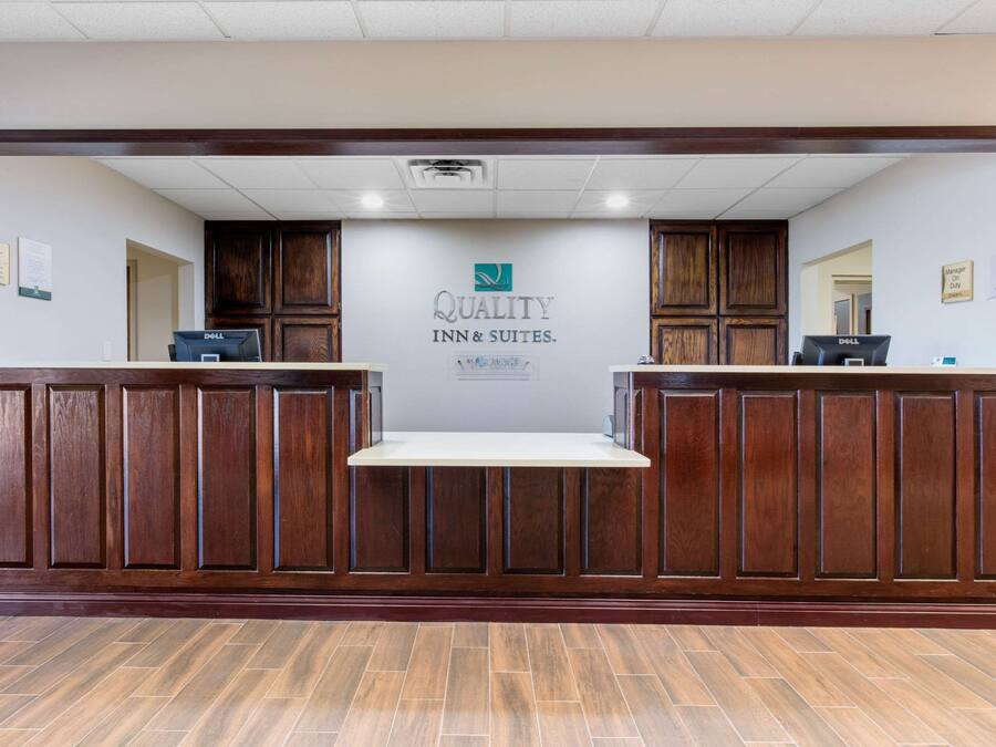 Una zona de recepción con un mostrador de madera, un letrero que dice “Quality Inn & Suites” y un piso de baldosas.