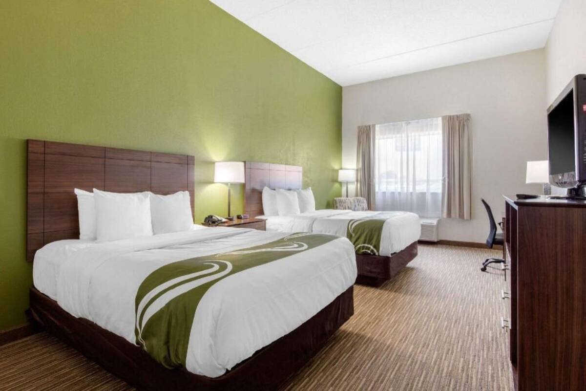 A hotel room with two beds, a desk, a TV, and a window with curtains.