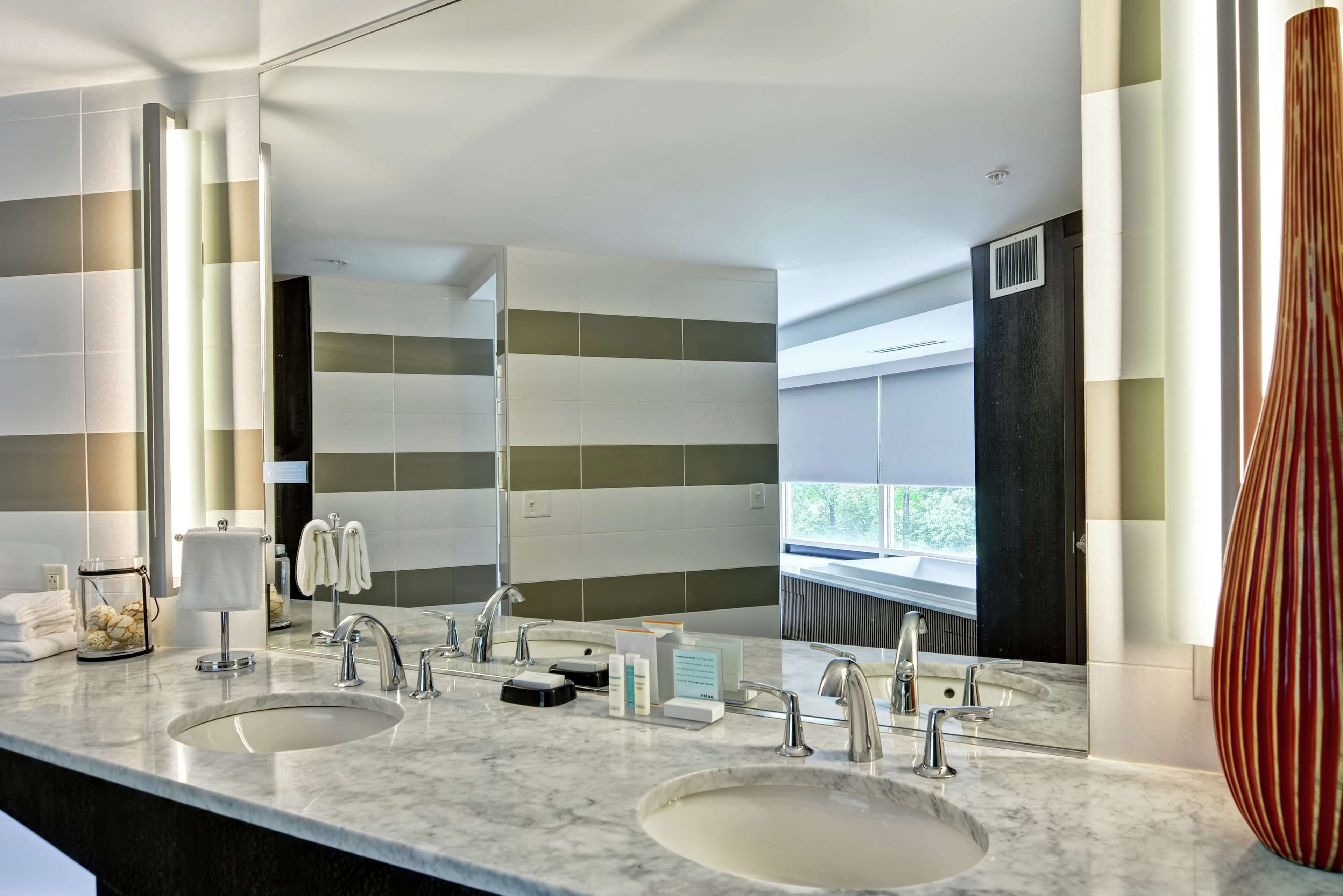 Une salle de bain moderne avec deux lavabos, un grand miroir et une vue sur l’extérieur.