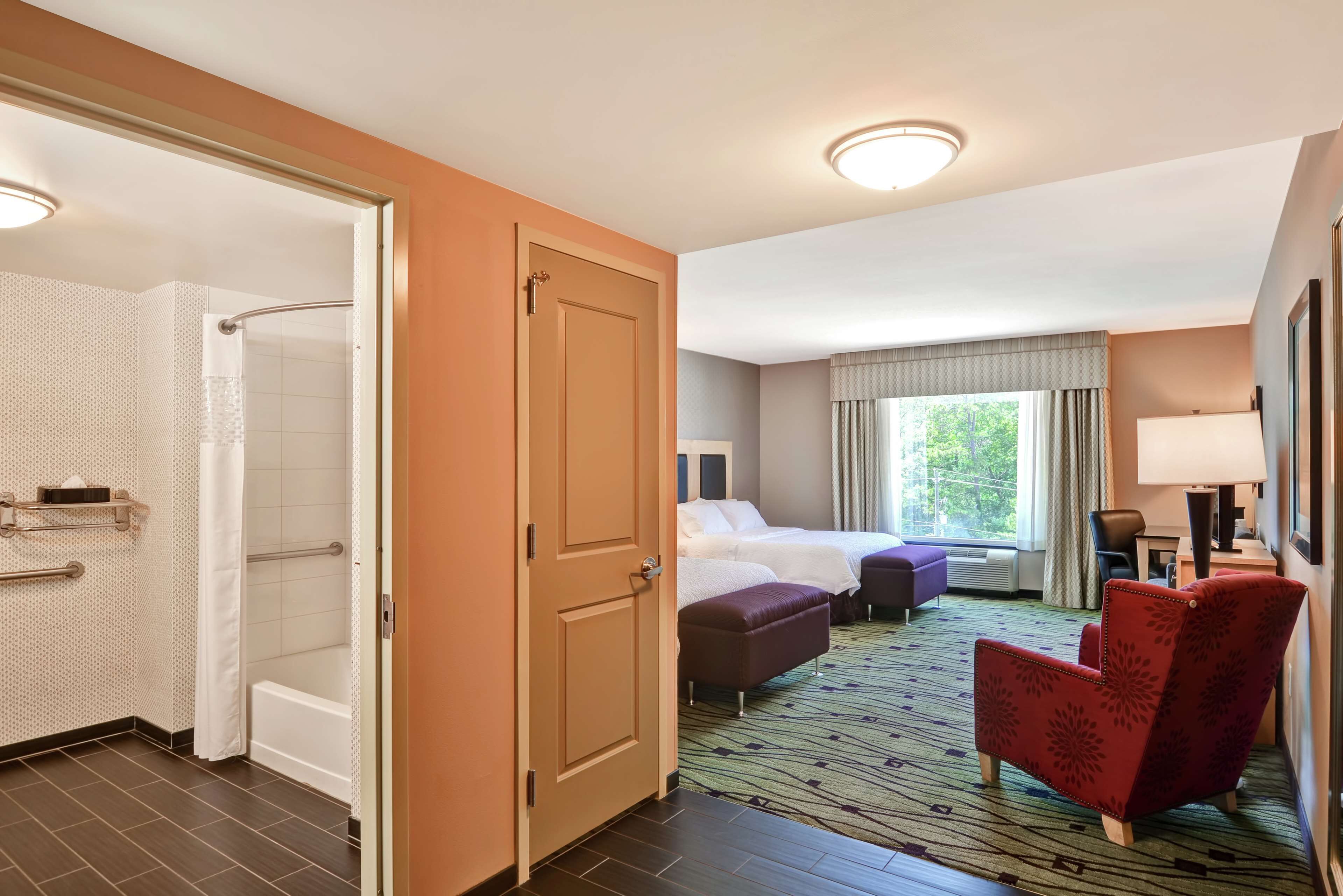 A hotel room with a shower, a bed, a red armchair, and a window with curtains.