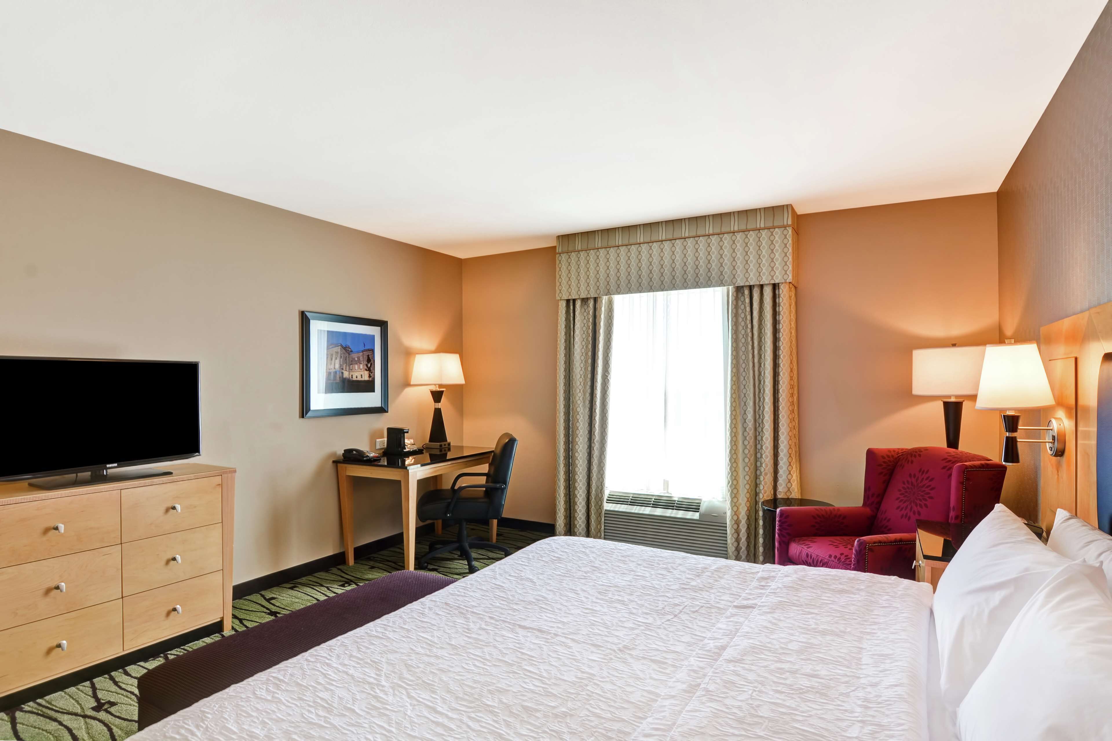A hotel room with a large bed, a desk with a chair, a television, and two lamps.