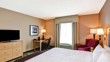 A hotel room with a large bed, a desk with a chair, a television, and two lamps.