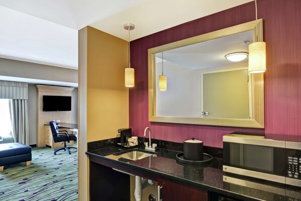 Une salle de bain d’hôtel avec un grand miroir, un lavabo, un four à micro-ondes et une chaise.