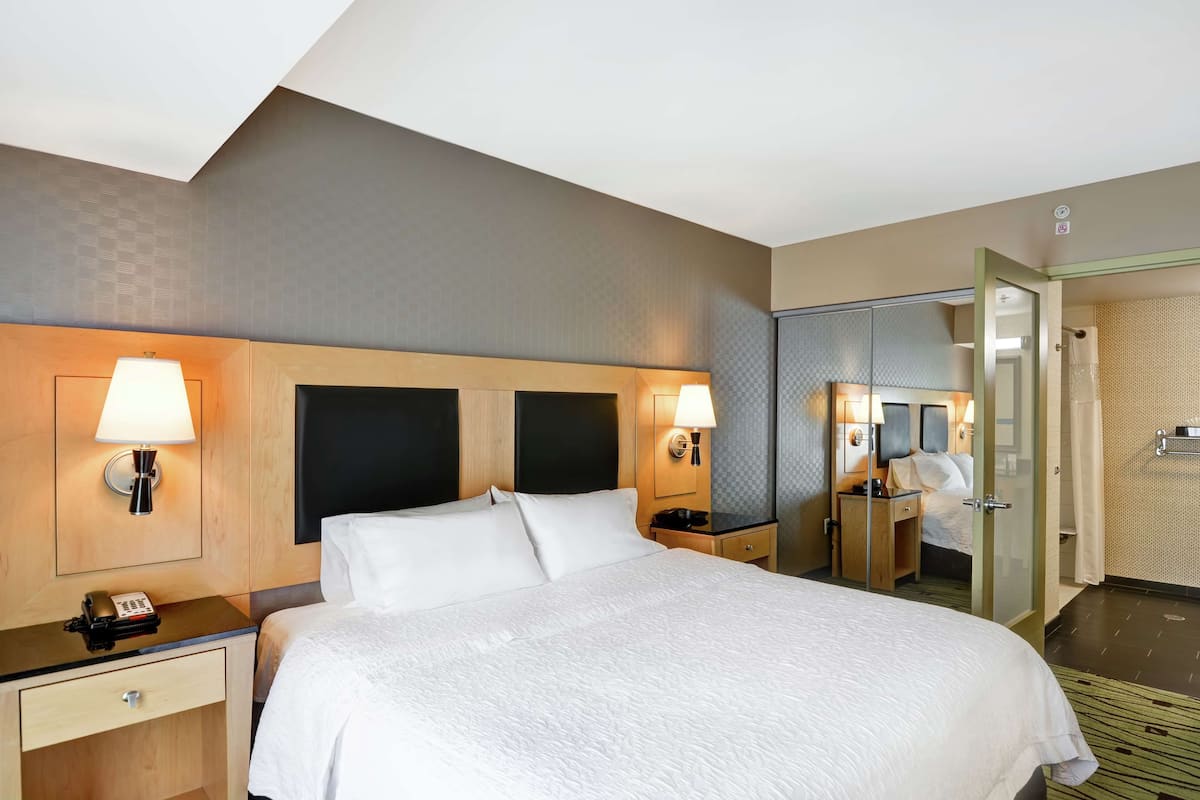 A hotel room with a large bed, bedside lamps, a nightstand, a mirror, and a bathroom visible through an open door.