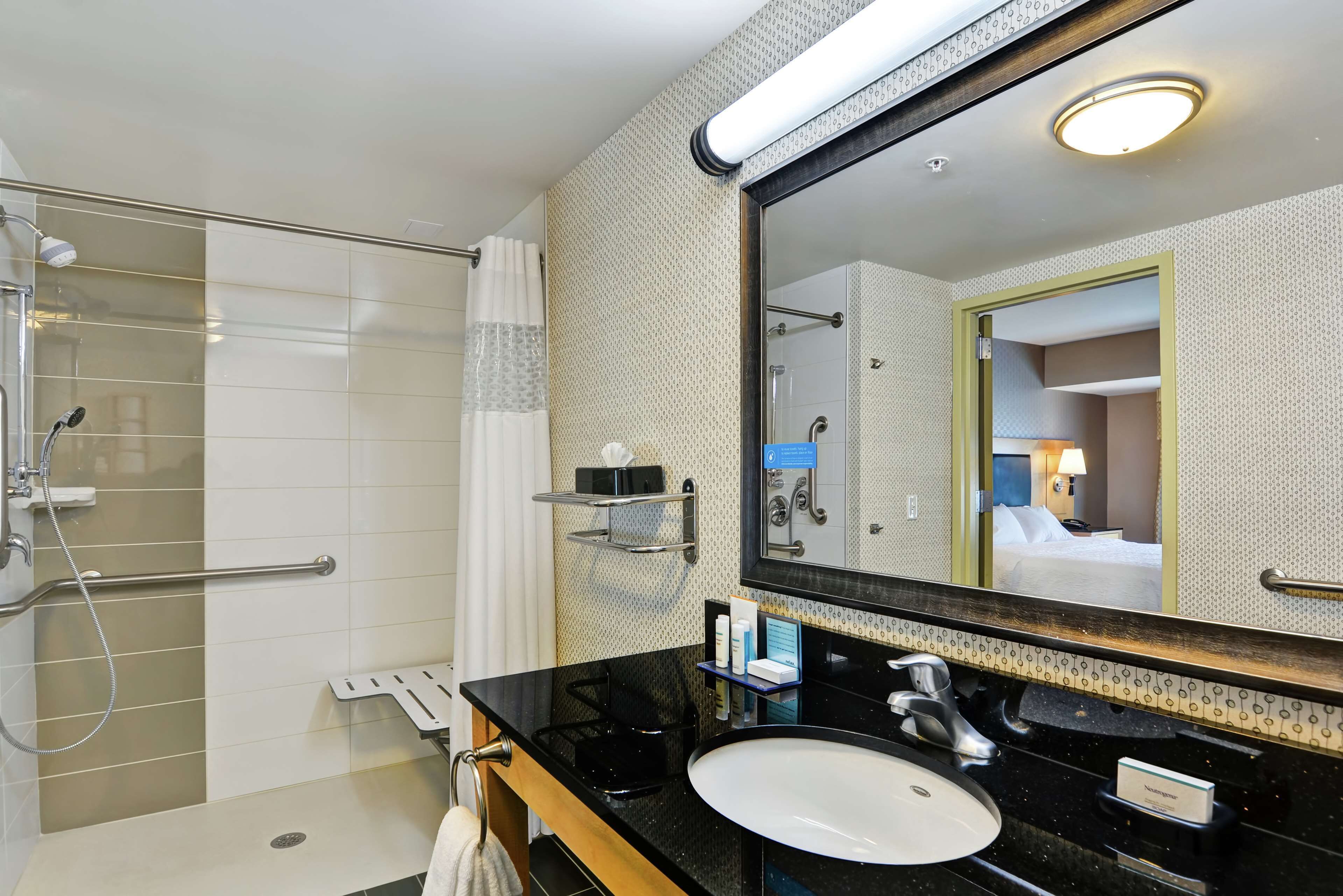 Un baño moderno con un lavabo negro, un espejo grande y una zona de ducha.