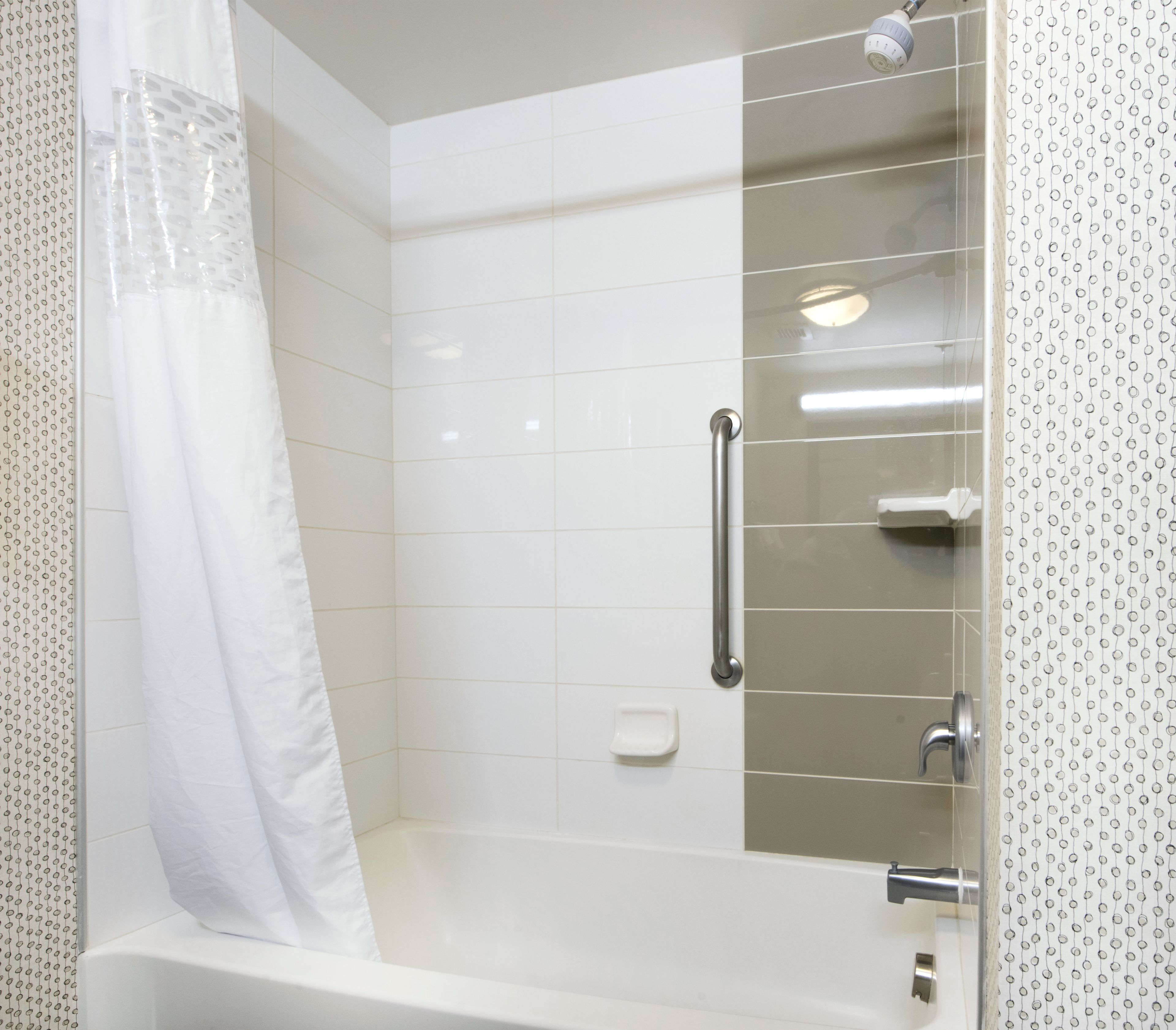 Un baño moderno con ducha, barra de apoyo y jabonera.