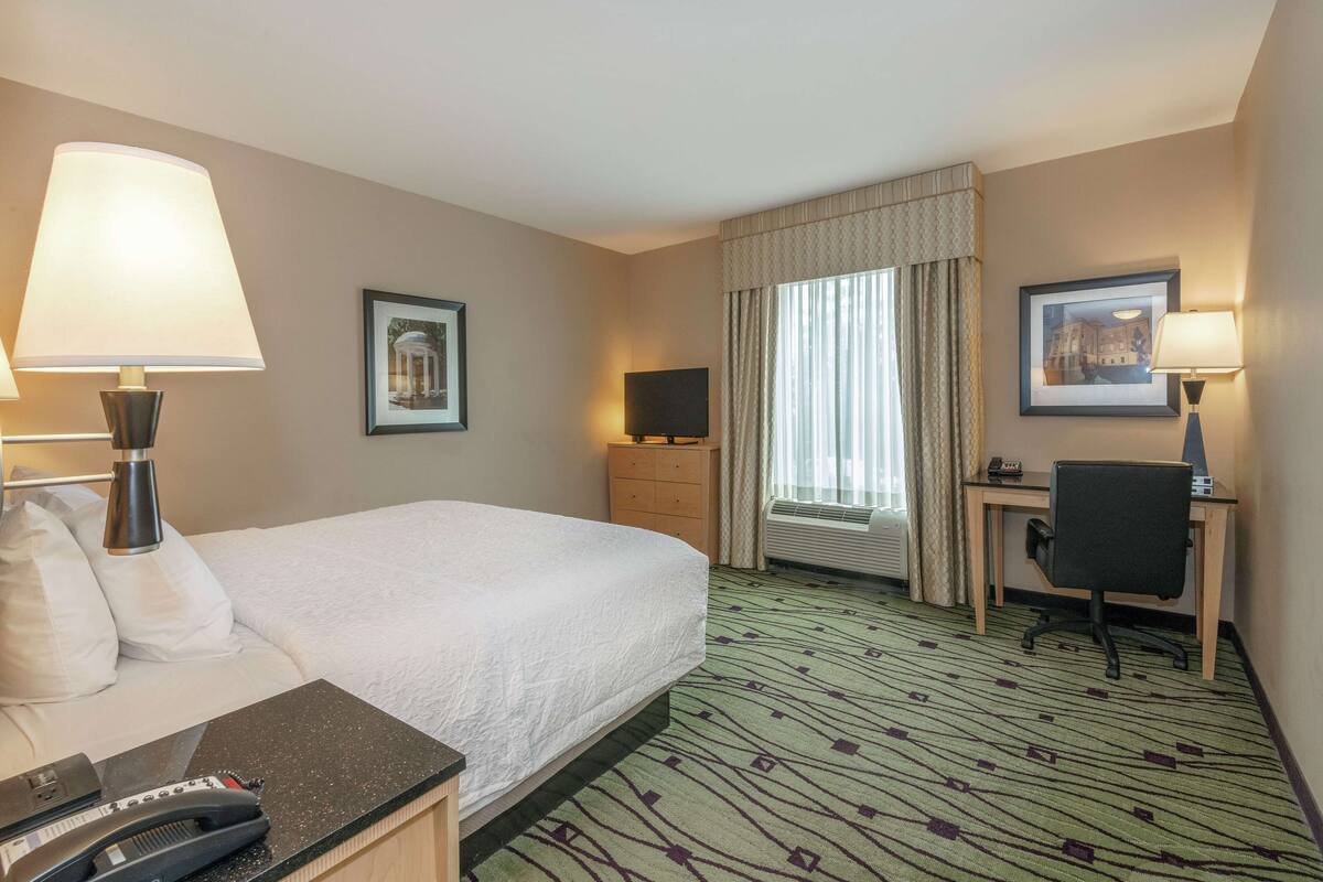 A hotel room with a bed, desk, chair, and two lamps.
