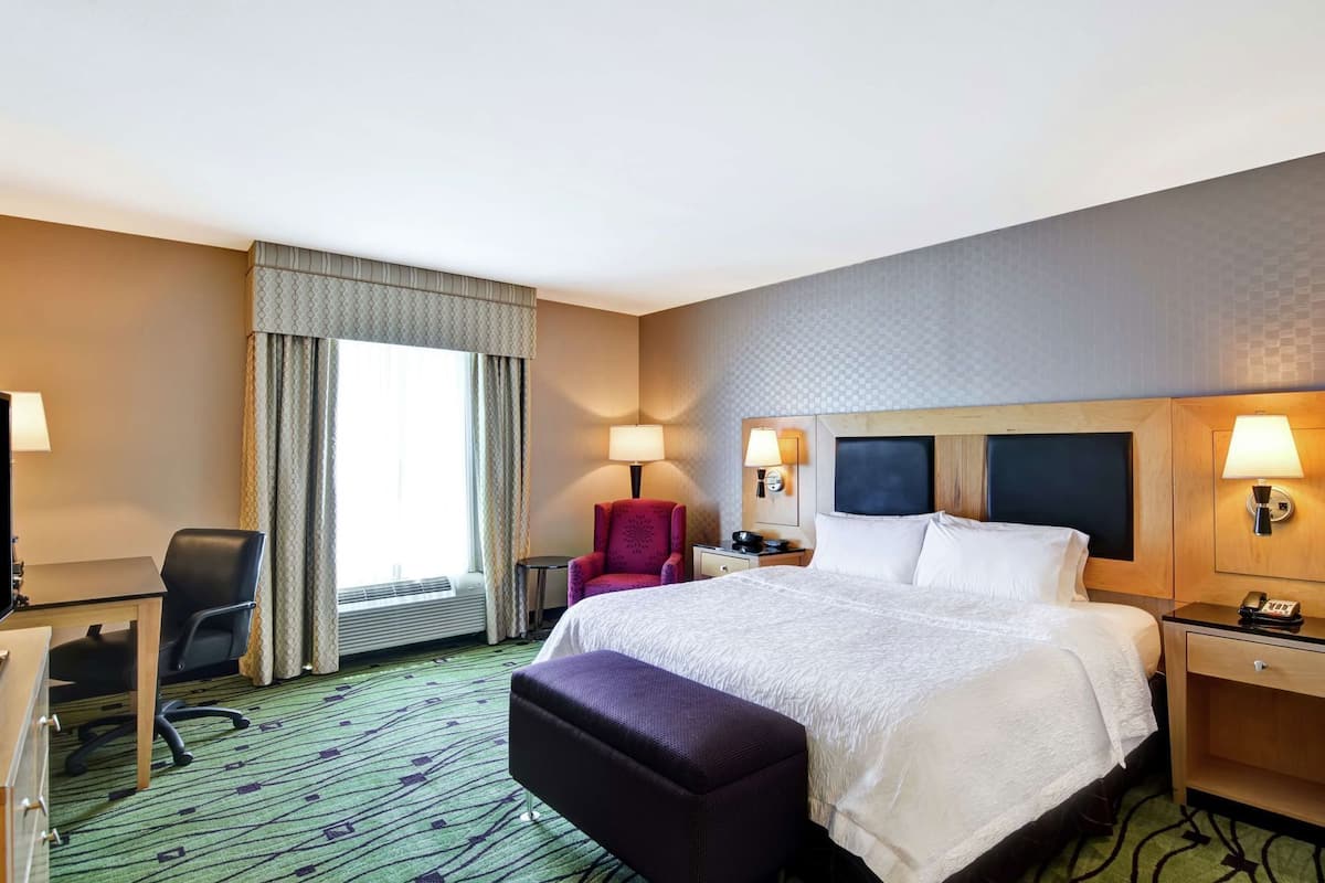 A hotel room with a bed, desk, chair, and a window with curtains.