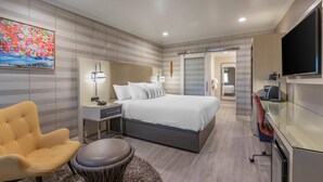 Une chambre d’hôtel moderne équipée d’un lit, d’une table de chevet, d’une lampe, d’une chaise, d’une table ronde et d’un téléviseur.