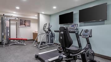 Une salle de sport équipée de matériel d’exercice, d’un tapis de course et d’un téléviseur fixé au mur.