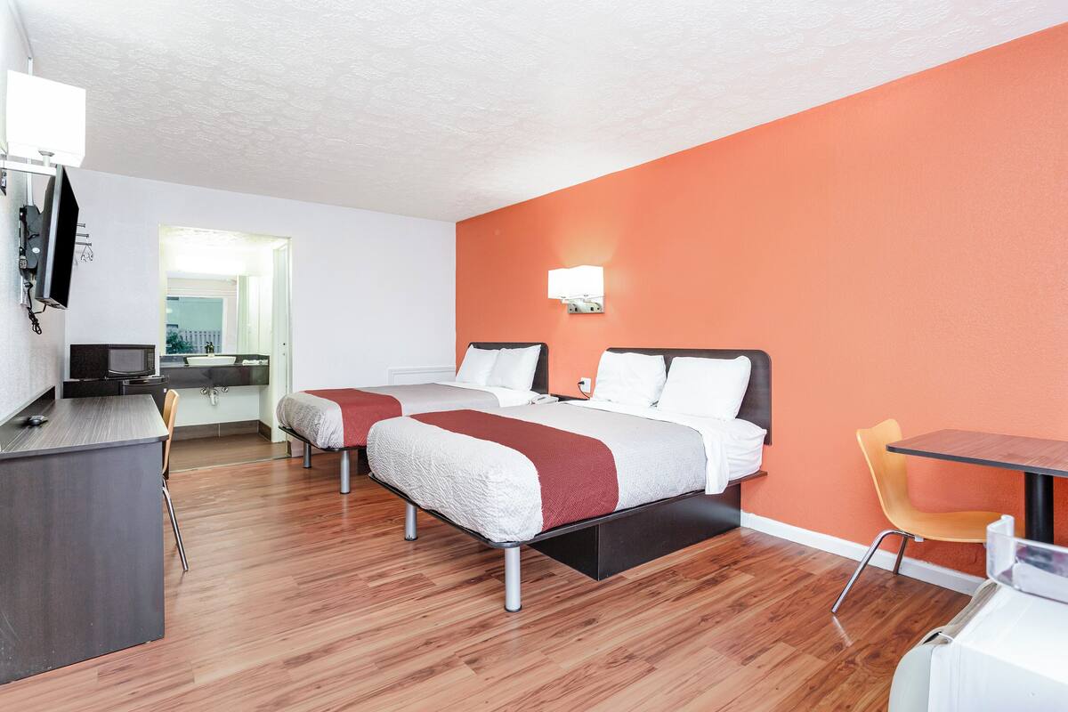 A hotel room with two beds, a desk, a chair, and a table.