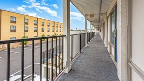 A covered corridor with a railing, leading to a building with multiple windows and an exit sign. - Relax Inn by OYO Columbus OH I 70 (Columbus)