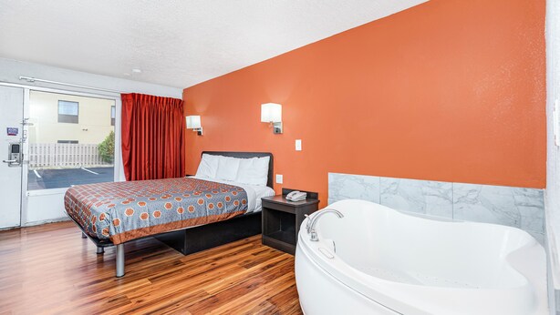 A bedroom with a bed, a nightstand, a white bathtub, and an orange wall. - Relax Inn by OYO Columbus OH I 70 (Columbus)