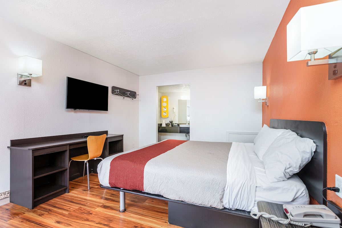 A hotel room with a bed, desk, chair, TV, and a bathroom visible through an open door.
