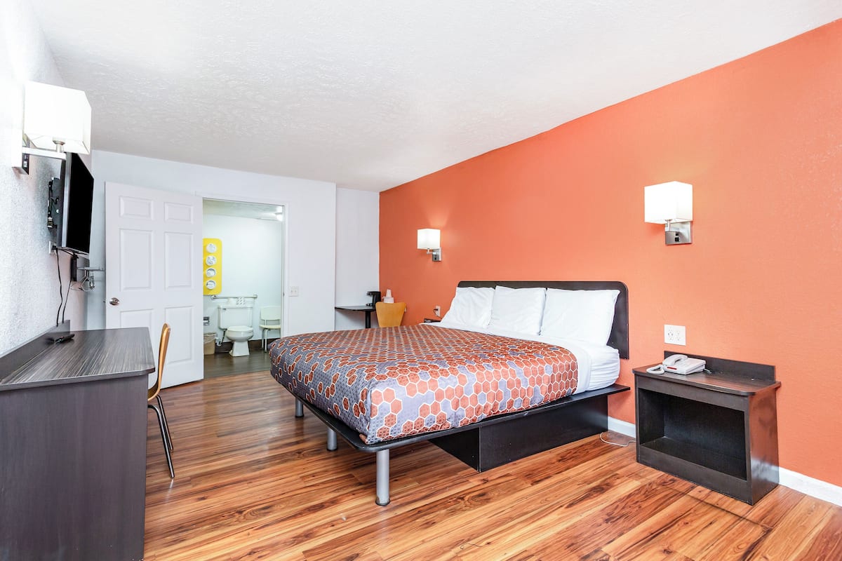 A hotel room with a bed, bedside table, and a desk with a chair.