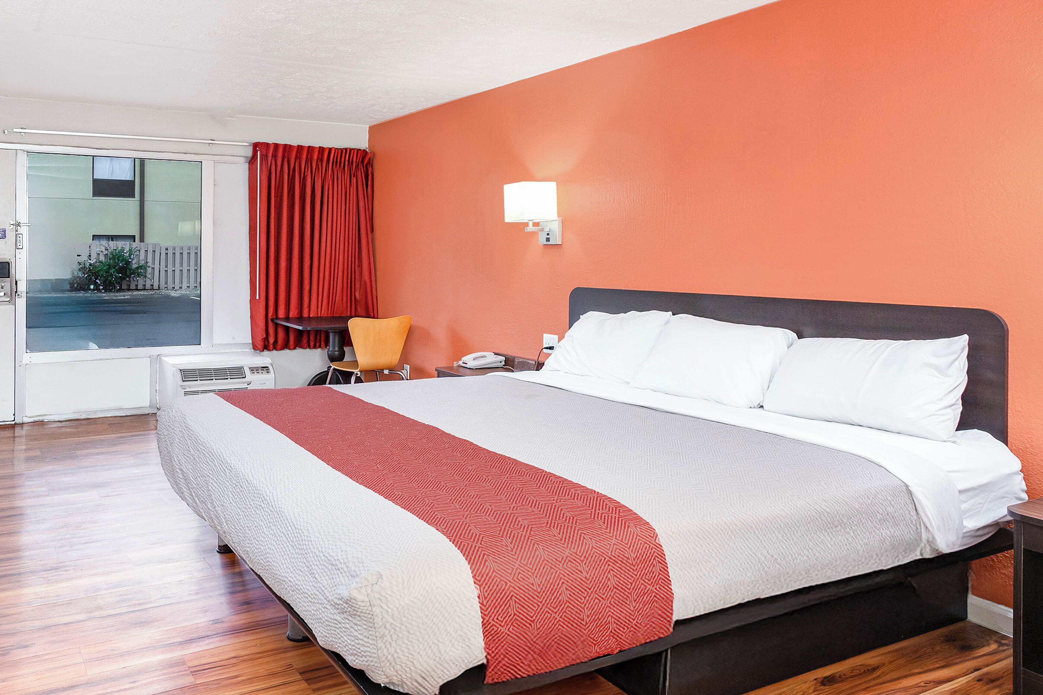 Una camera d'albergo con un letto, una scrivania, una sedia e una finestra con tende.