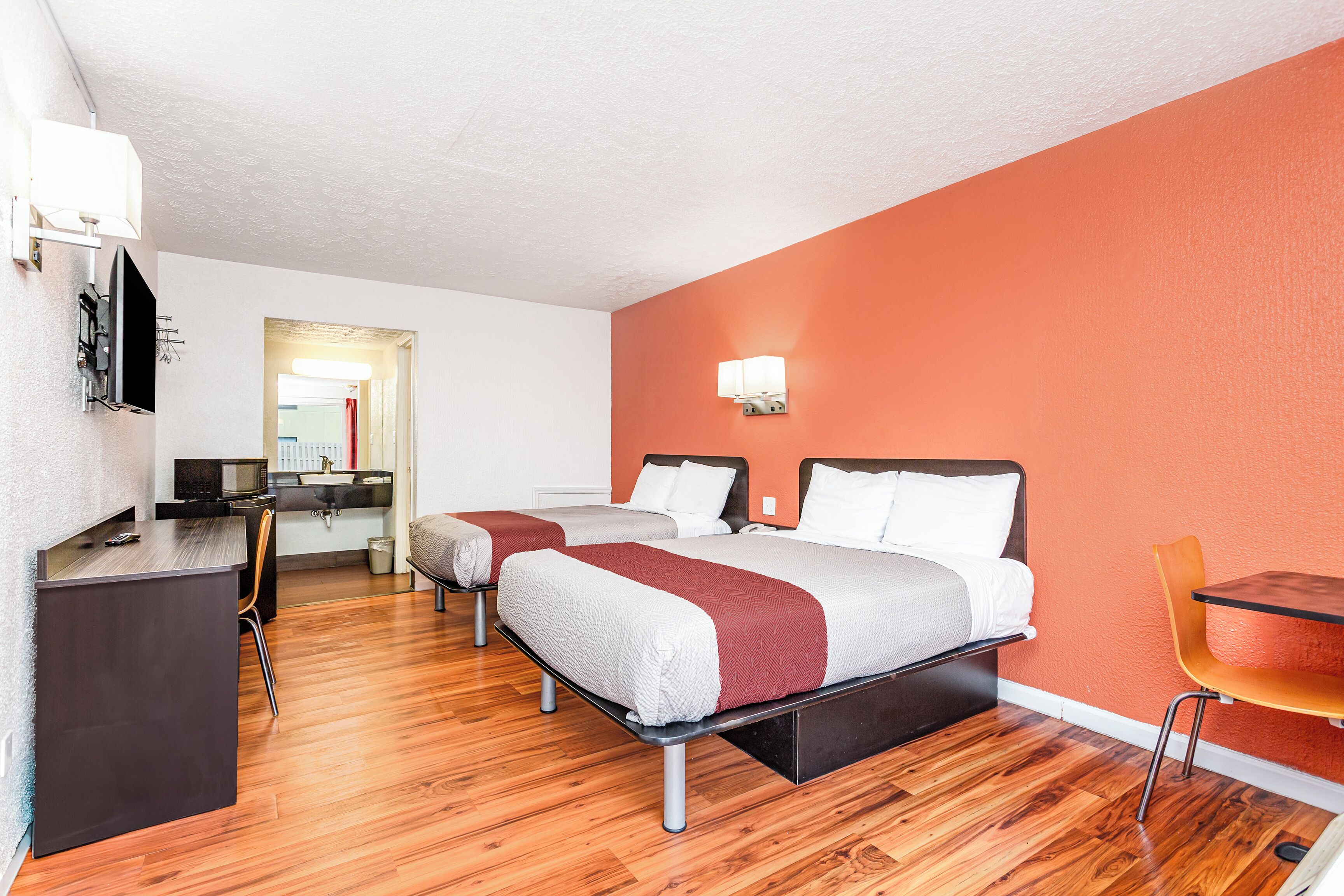 A hotel room with two beds, a desk, a chair, and a TV.