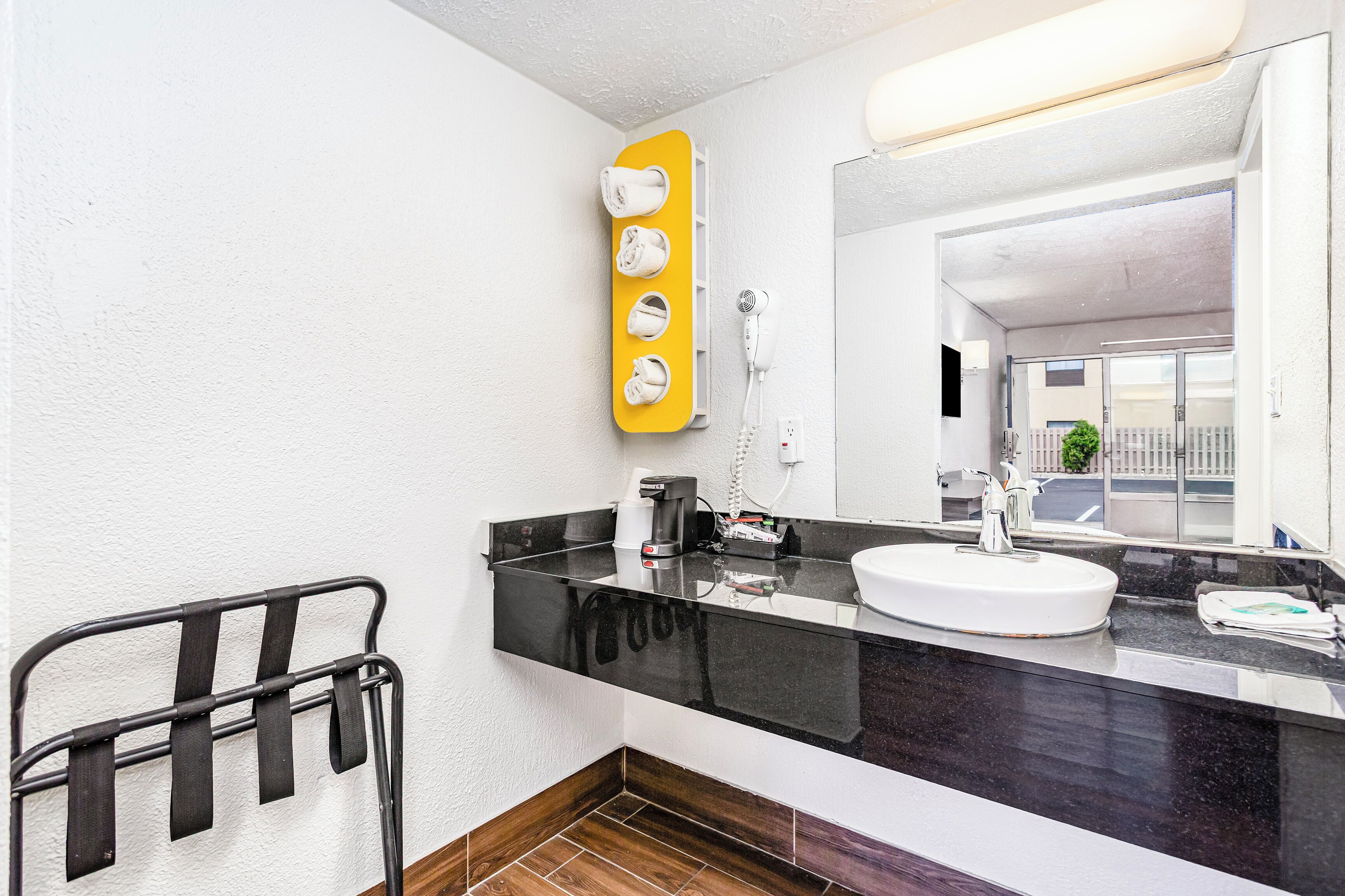 A bathroom with a black countertop, a white sink, a mirror, and a towel rack with towels.