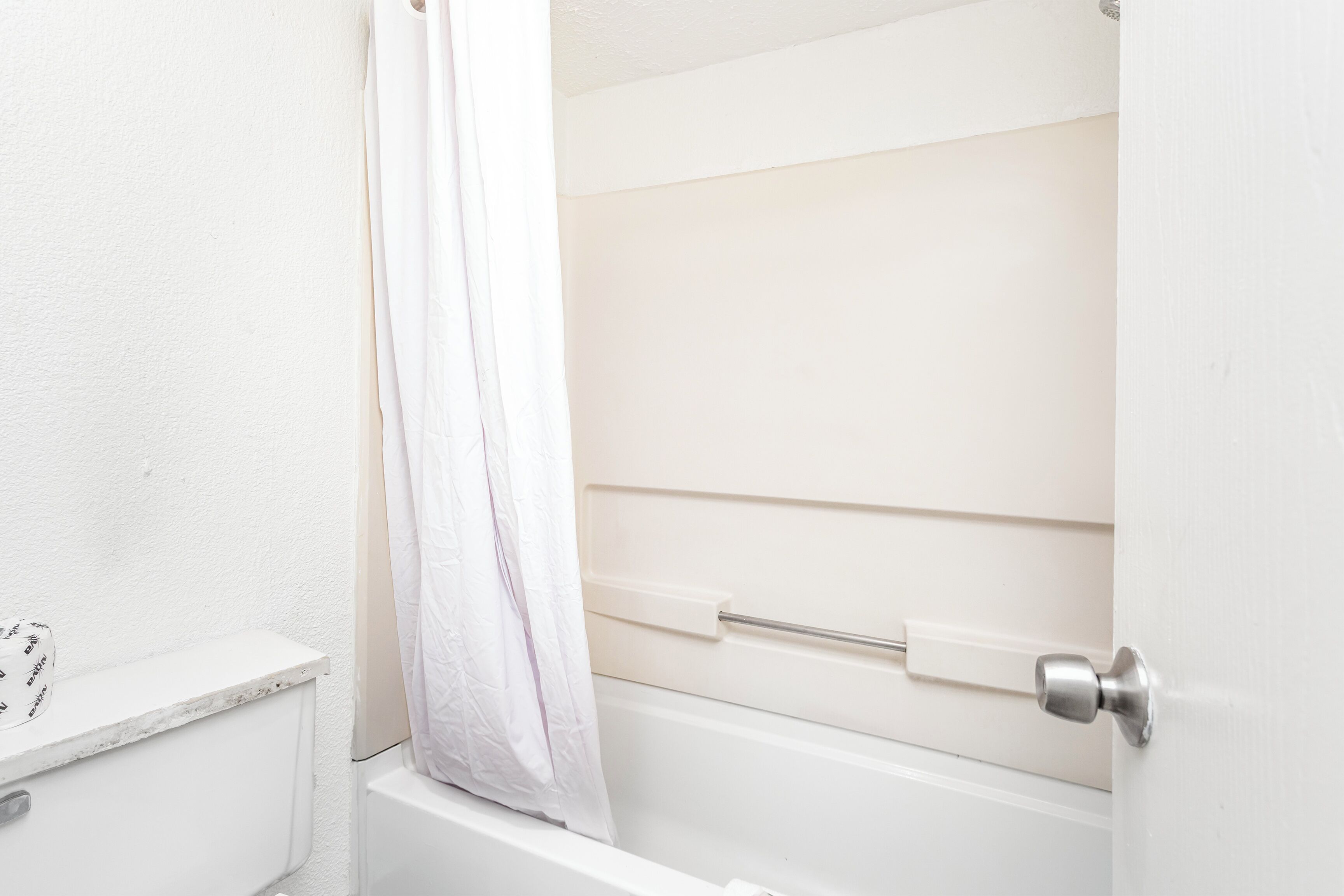 Ein helles Badezimmer mit einer Badewanne, einer Duschvorhang und einem Türgriff.