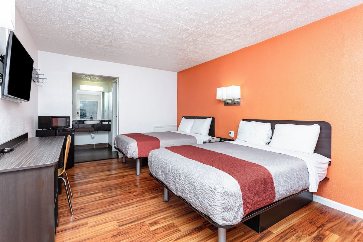 A hotel room with two beds, a desk, a TV, and a bathroom visible through an open door.