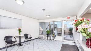 A clean, modern waiting area with two black chairs, a small round table, and a vase of flowers. - Relax Inn by OYO Columbus OH I 70 (Columbus)