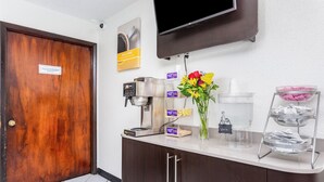 A hotel reception area with a wooden door, a coffee machine, a TV mounted on the wall, and a vase with flowers on the counter. - Relax Inn by OYO Columbus OH I 70 (Columbus)