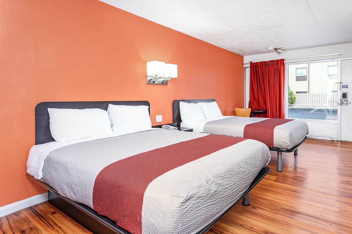A hotel room with two beds, a red curtain, a white wall, and a wooden floor.