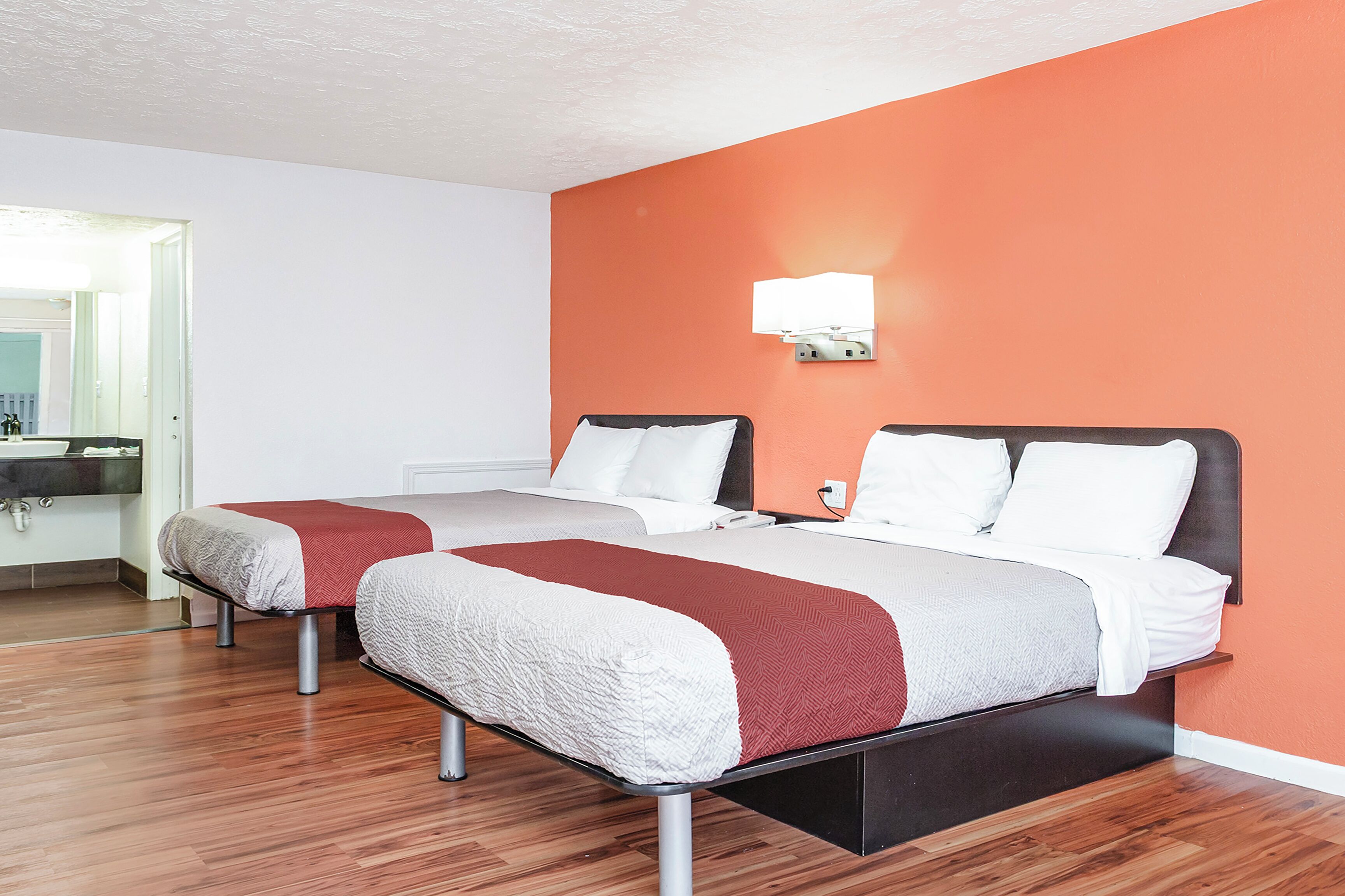 A hotel room with two beds, a bathroom, and a mirror.