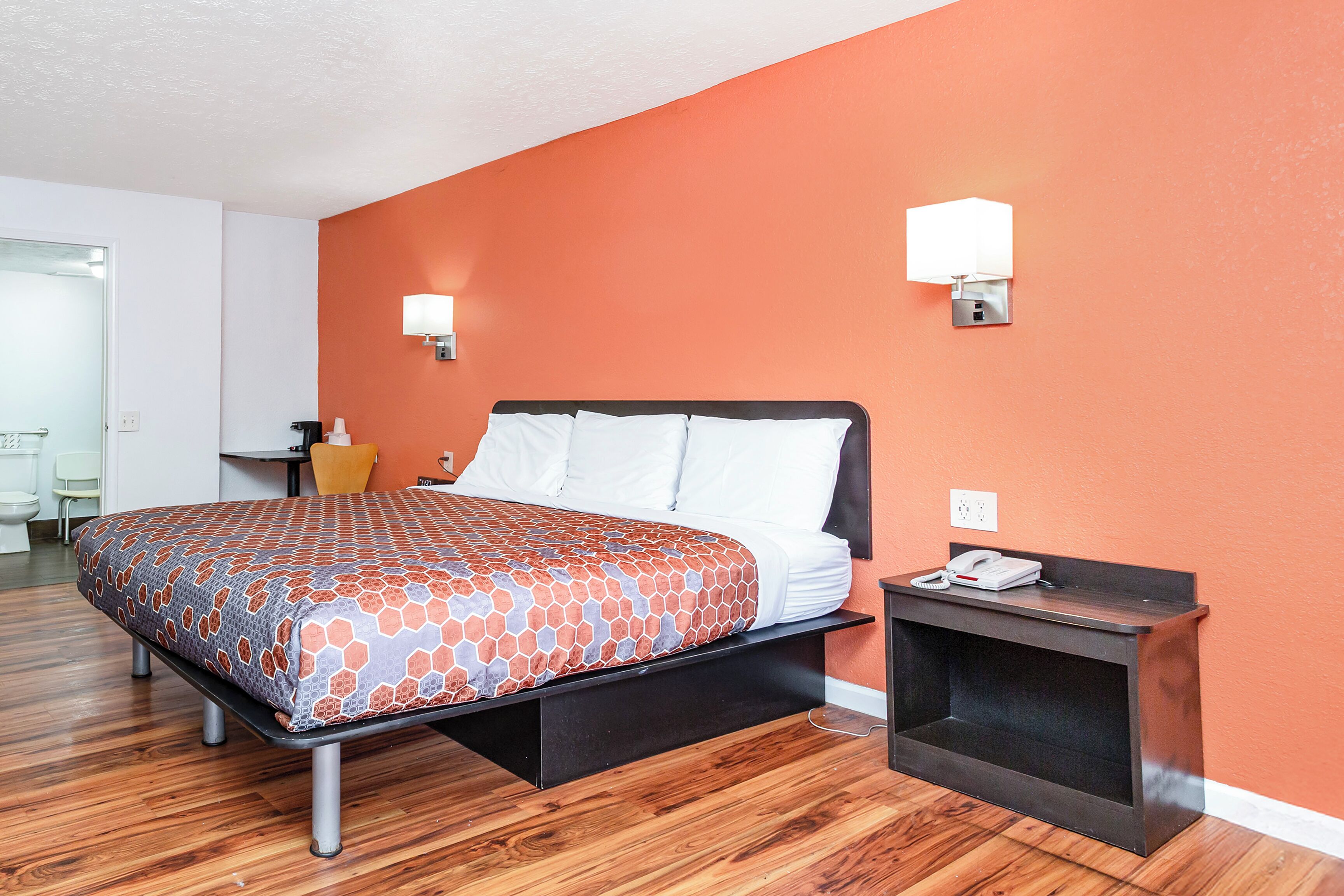 A hotel room with a bed, a nightstand, and a wall-mounted lamp.